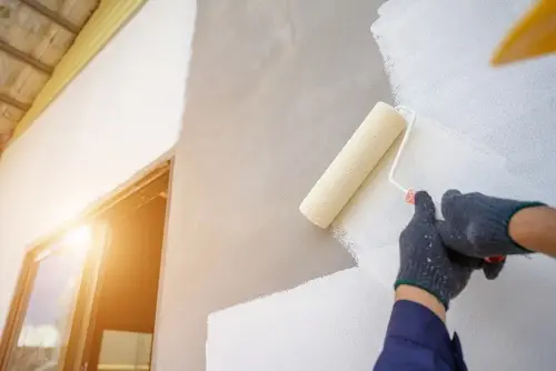 Professional painter applying primer with roller on house exterior.