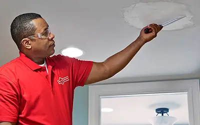 A Mr. Handyman service professional repairing ceiling drywall.