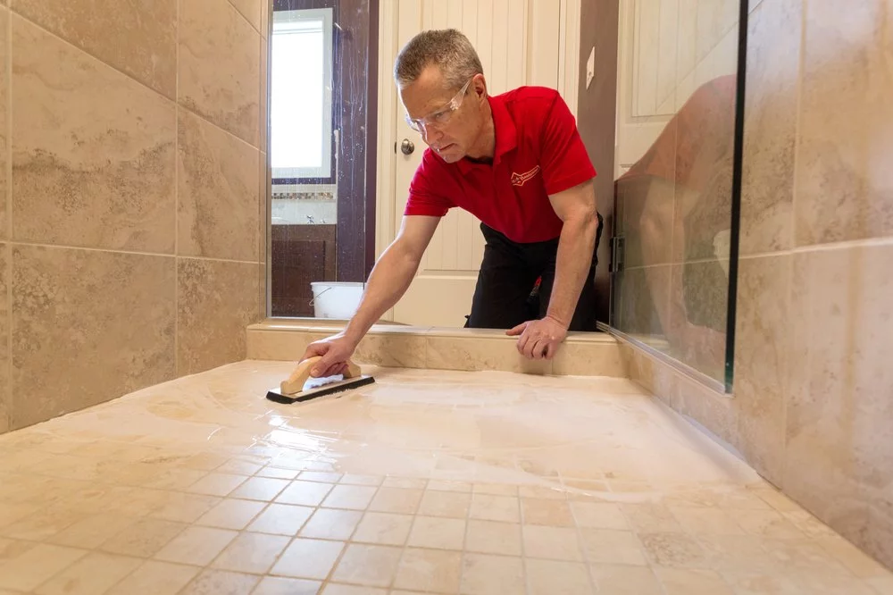 A Mr. Handyman technician applying grout to a new shower tile floor.