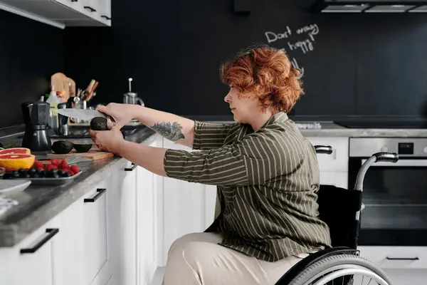 Woman in a wheelchair cuts avocado in kitchen.