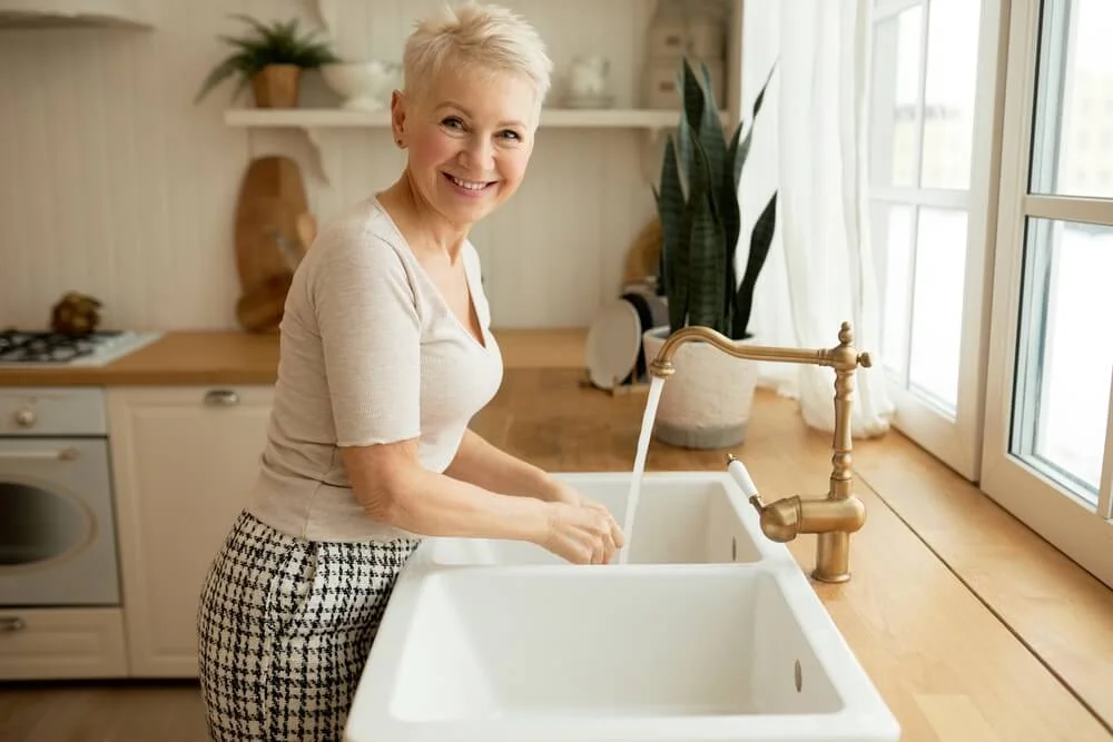 A woman washing hands in the kitchen sink.