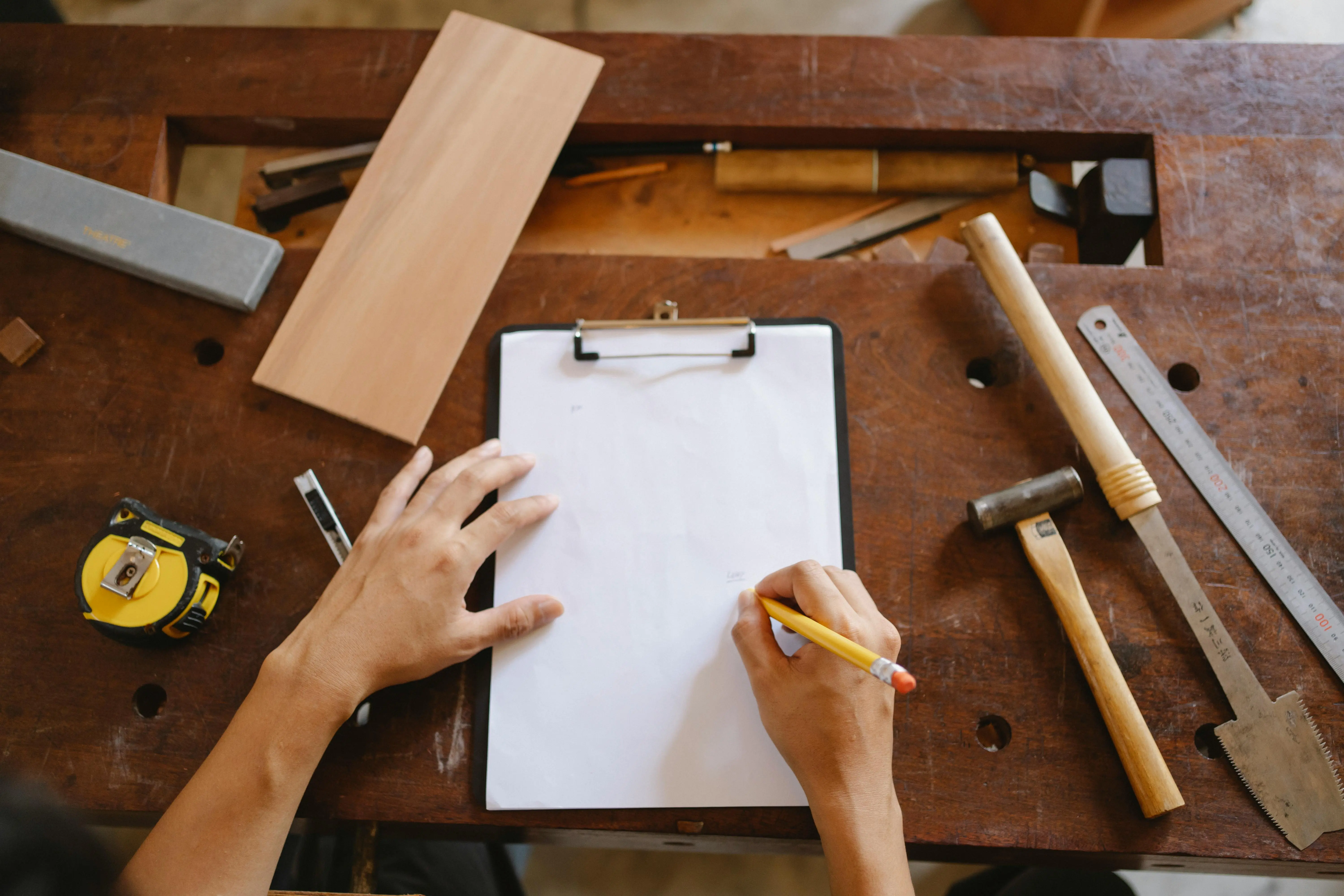 A handyman writing on a piece of paper on a clipboard surrounded by tools.