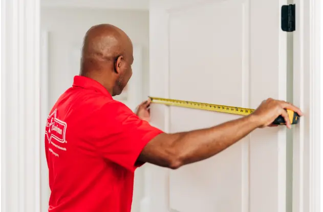 Mr. Handyman professional using a measuring tape to measure the width of a door.