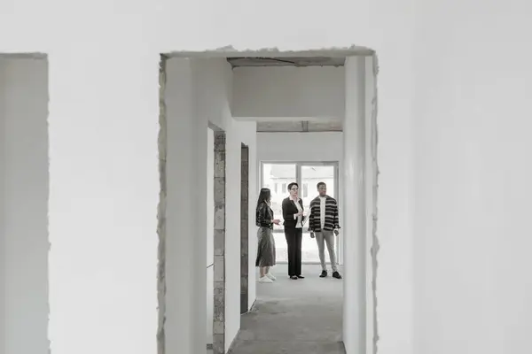 A couple stands next to a realtor in the hallway of a house.