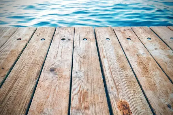 Brown planks for a deck extend over blue water.
