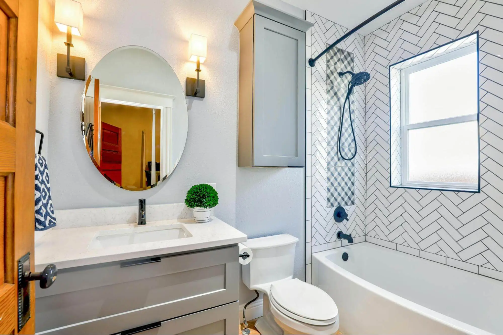 A white bathroom with a tiled shower. it is brightly lit and features a white sink, white toilet, and a round mirror.