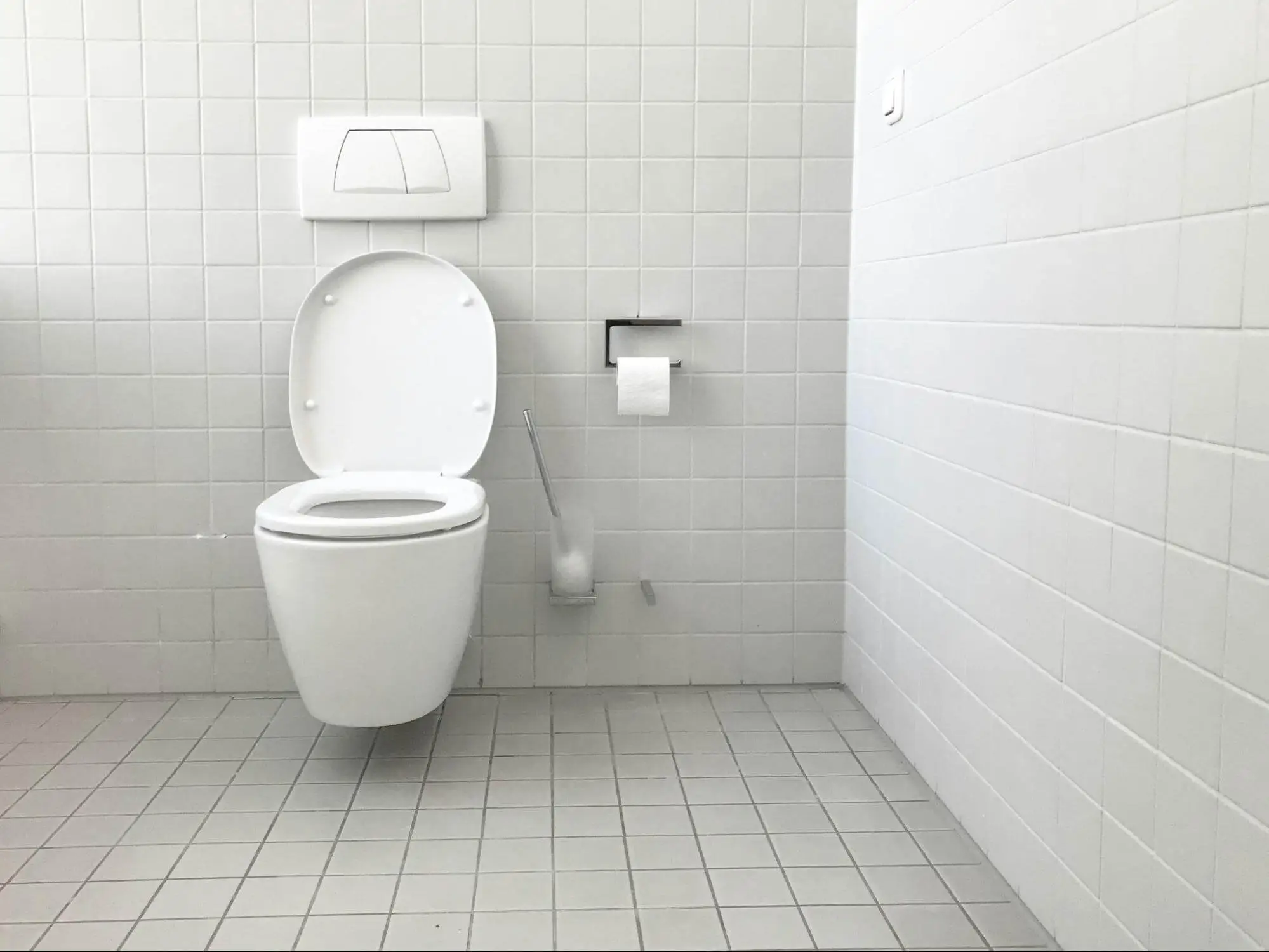 A white toilet in an all white tiled bathroom.