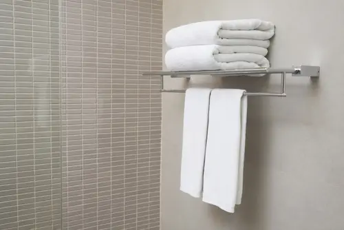 White towels on a towel rack installed on a tile wall.