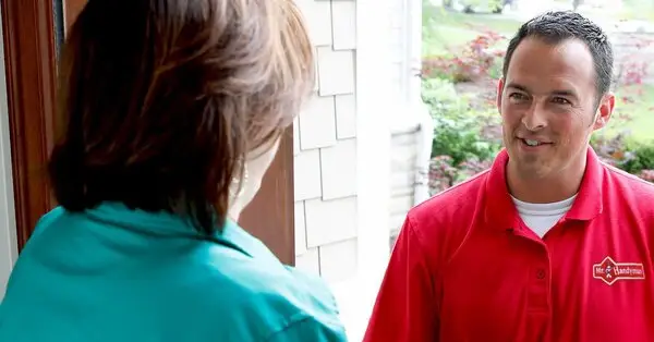 A smiling handyman from Mr. Handyman speaking with a homeowner at their front door.