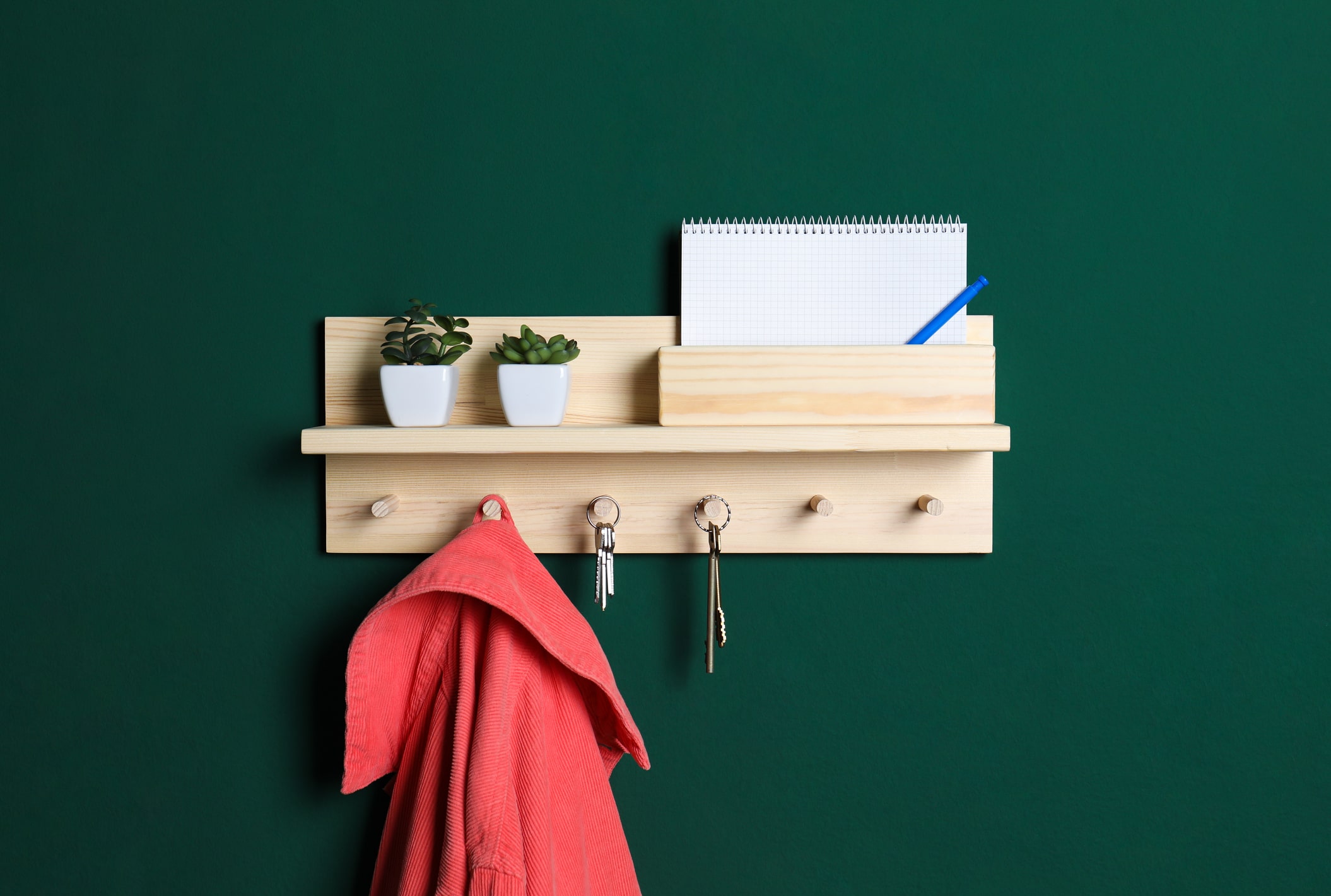 A shelf hung on a green wall with keys and jacket.